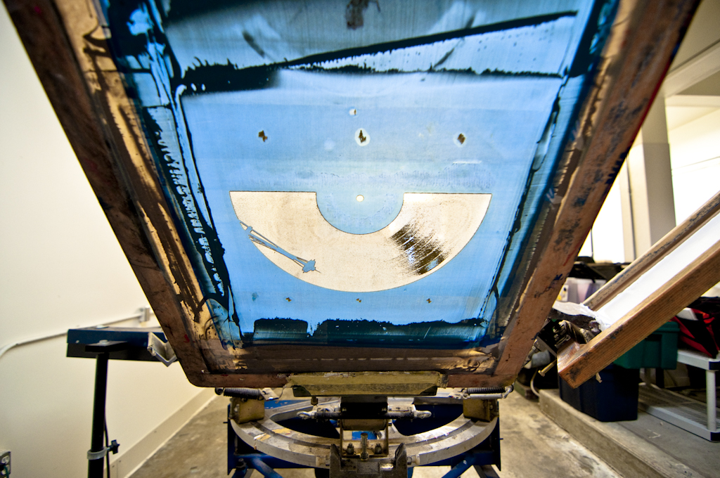 Screen with design exposed, blue emulsion, screenprint press