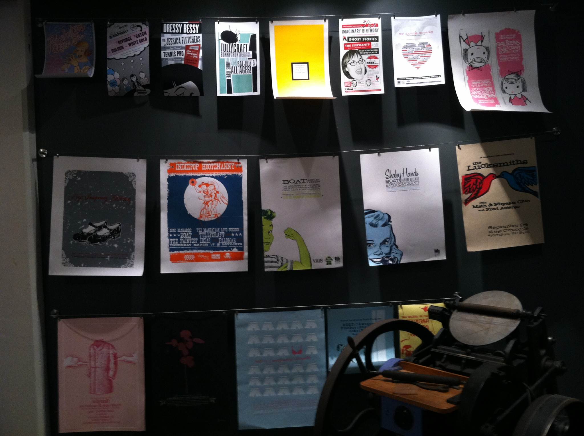 Dark display wall with posters on rails and letterpress in corner